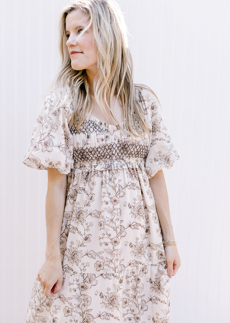 Model wearing a cream dress with brown floral, bubble short sleeves and a smocked bust. 