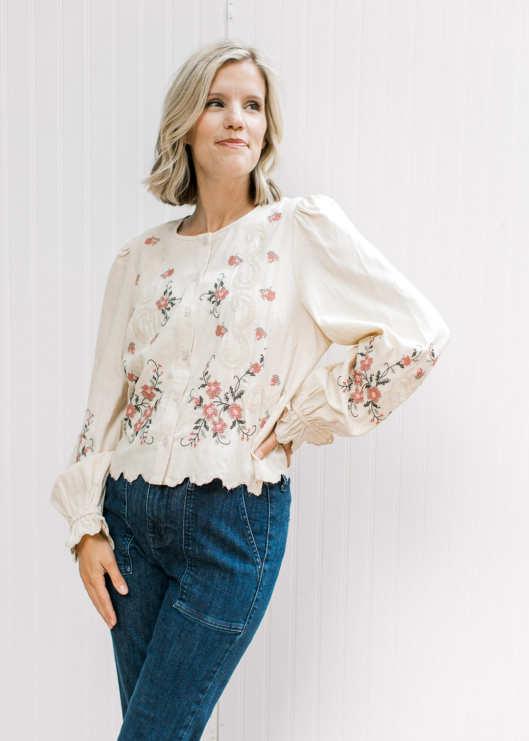 Model wearing a taupe top with floral, buttons, long poet sleeves and scalloped hem.