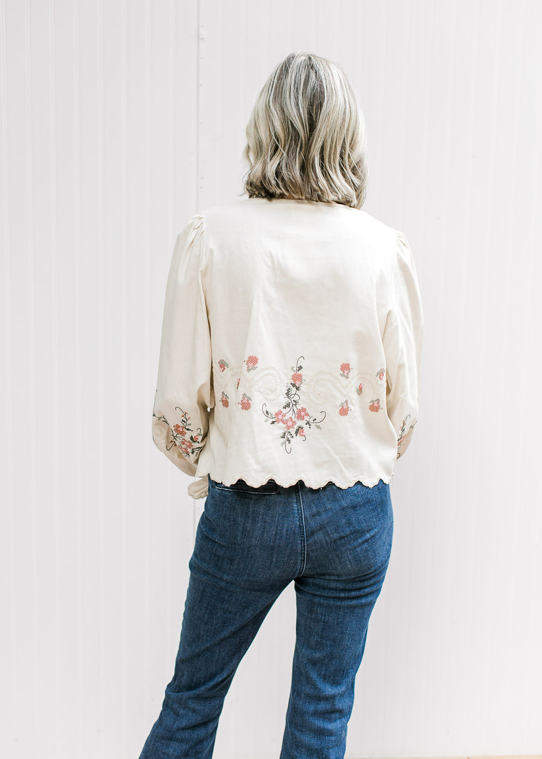 Back view of Model wearing a taupe top with floral, buttons, long poet sleeves and scalloped hem.