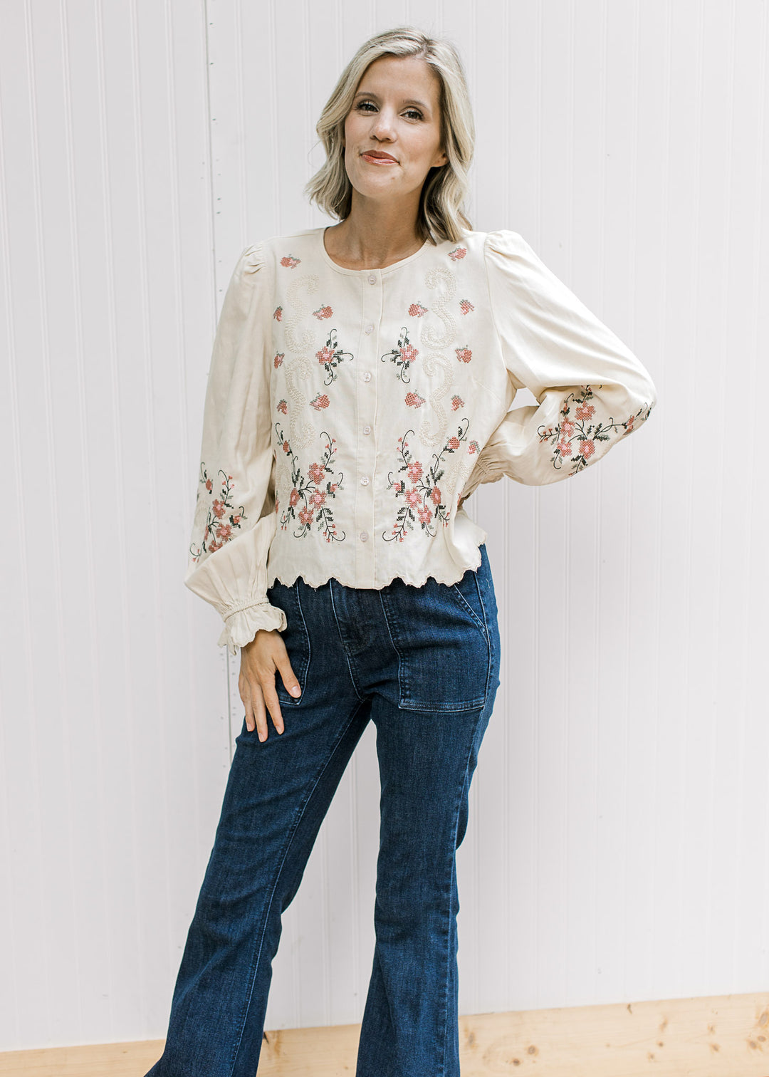 Model wearing jeans and a taupe top with floral, buttons, long poet sleeves and scalloped hem.