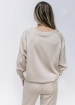Back view of Model wearing a classic taupe sweatshirt with a round neck and long sleeves.