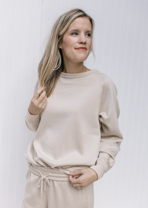 Model wearing a classic taupe lightweight sweatshirt with a round neck and long sleeves. 