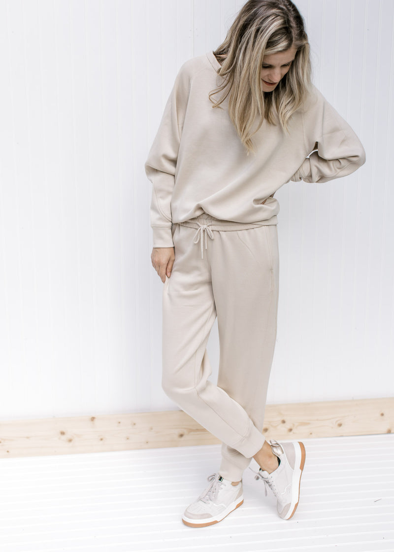 Model wearing sneakers and taupe joggers with a matching long sleeve sweatshirt with a round neck. 