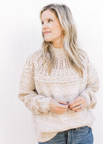 Model wearing an oatmeal colored sweater with open knit yolk detail and a mock neck. 