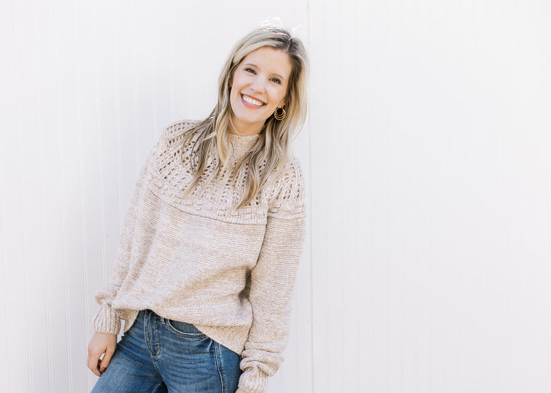 Model wearing jeans and an oatmeal colored sweater with open knit yolk detail and a mock neck. 