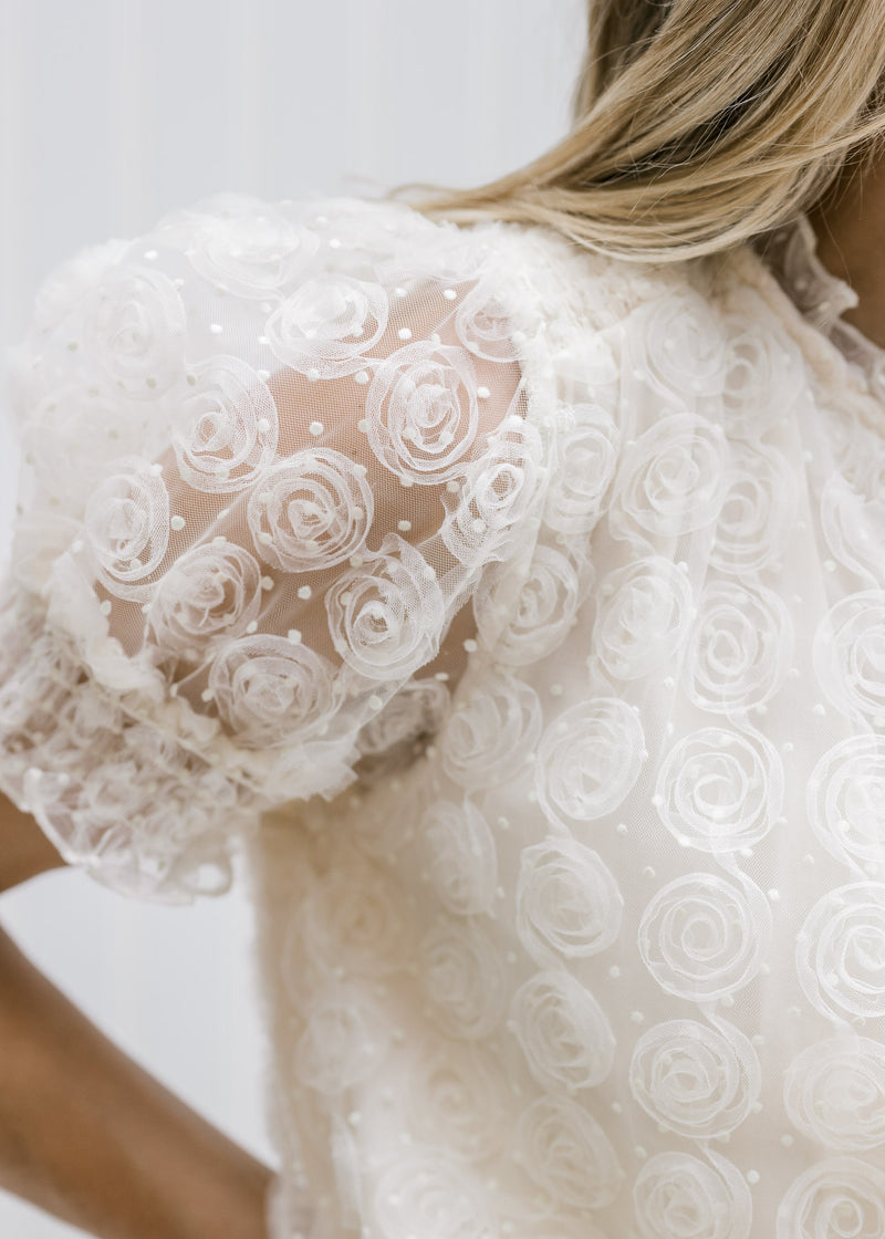 Close up of lace short puff sleeve with a floral design on a model in a cream top. 