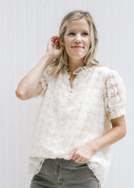 Model wearing a cream v-neck top with floral lace overlay and three button closure. 