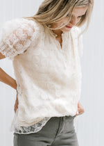 Model wearing a cream v-neck top with floral lace overlay and lace short sleeves. 