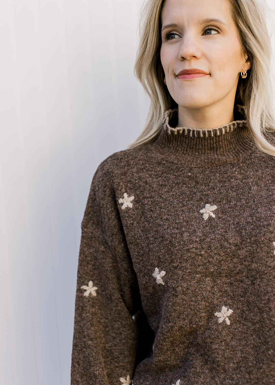 Close up of mock neckline with taupe stitching and taupe flowers on a brown sweater.