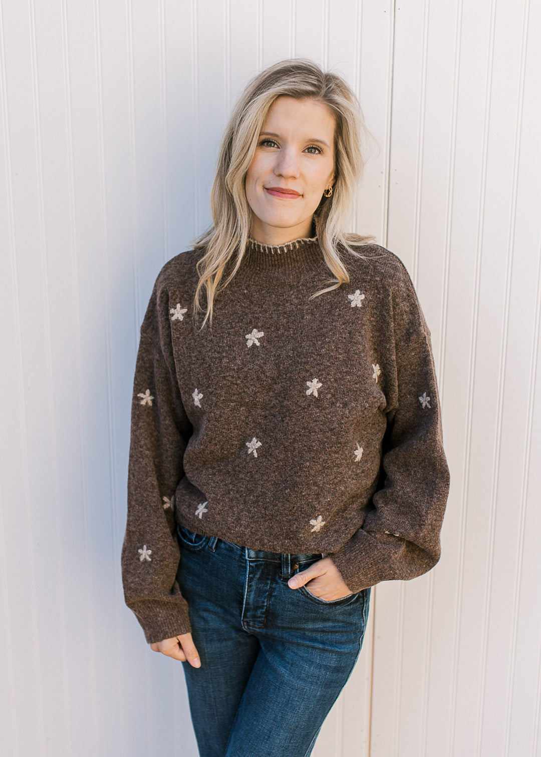 Model wearing a soft brown sweater with taupe stitched flowers, a mock neck and long sleeves. 