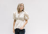 Model wearing a cream v-neck top with an elastic waistband and bubble short sleeves. 