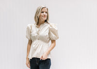 Model wearing a cream v-neck top with an elastic waistband and bubble short sleeves. 