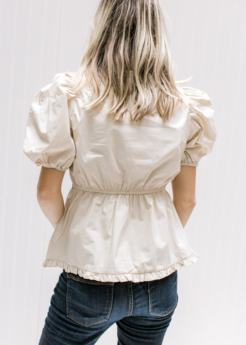 Back view of cream top with an elastic waistband, bubble short sleeves and ruffle detail on v-neck.