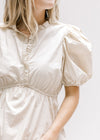 Close up of bubble short sleeve and ruffle detail at v-neck of a cream top with an elastic waist. 
