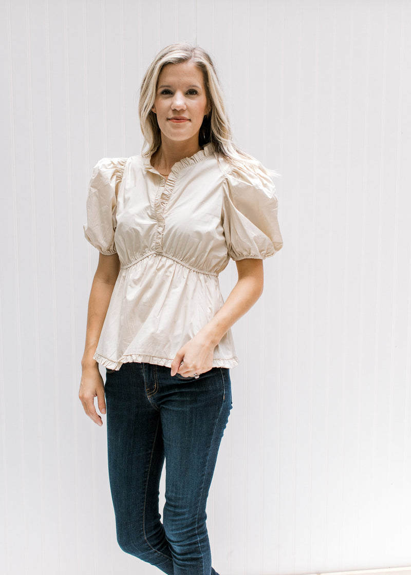 Model wearing jeans with a cream top with an elastic waist, bubble short sleeves and v-neck. 