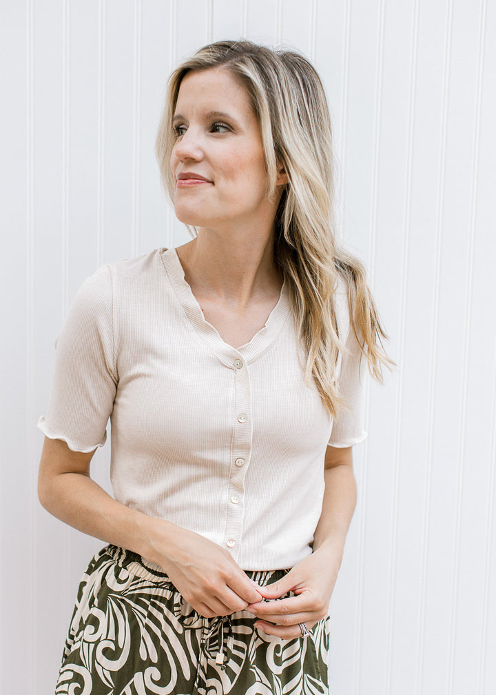 Model wearing an oatmeal ribbed top with faux pearl button front, v-neck and short sleeves.