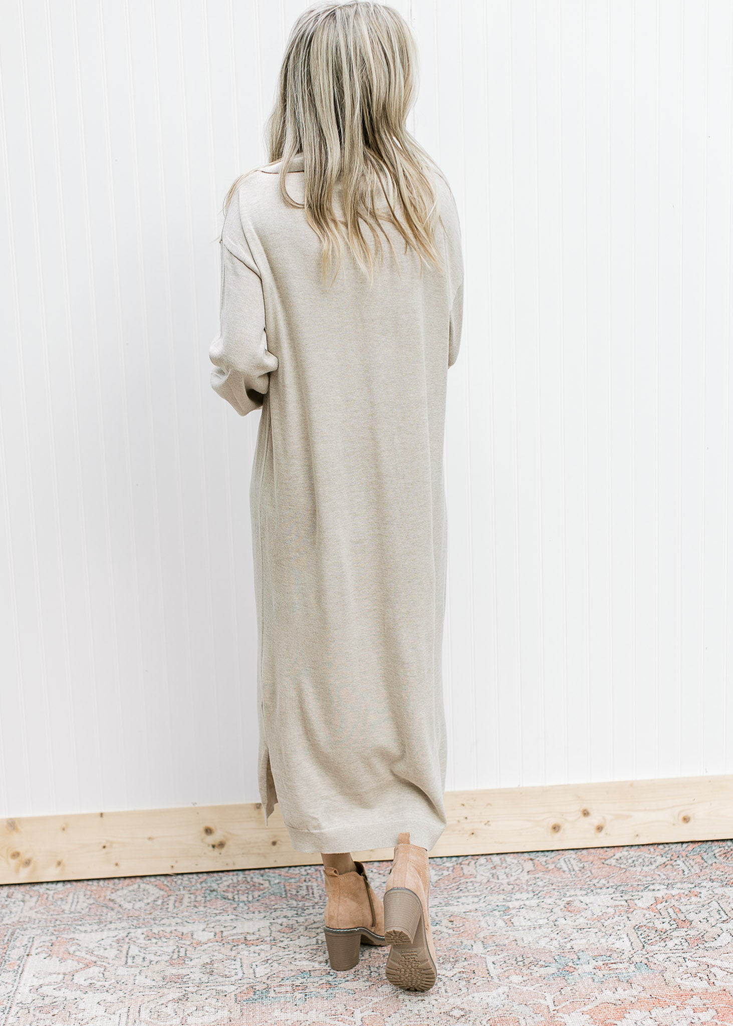 Back view of Model wearing a wheat colored midi with long sleeves, v-neck and exaggerated collar. 