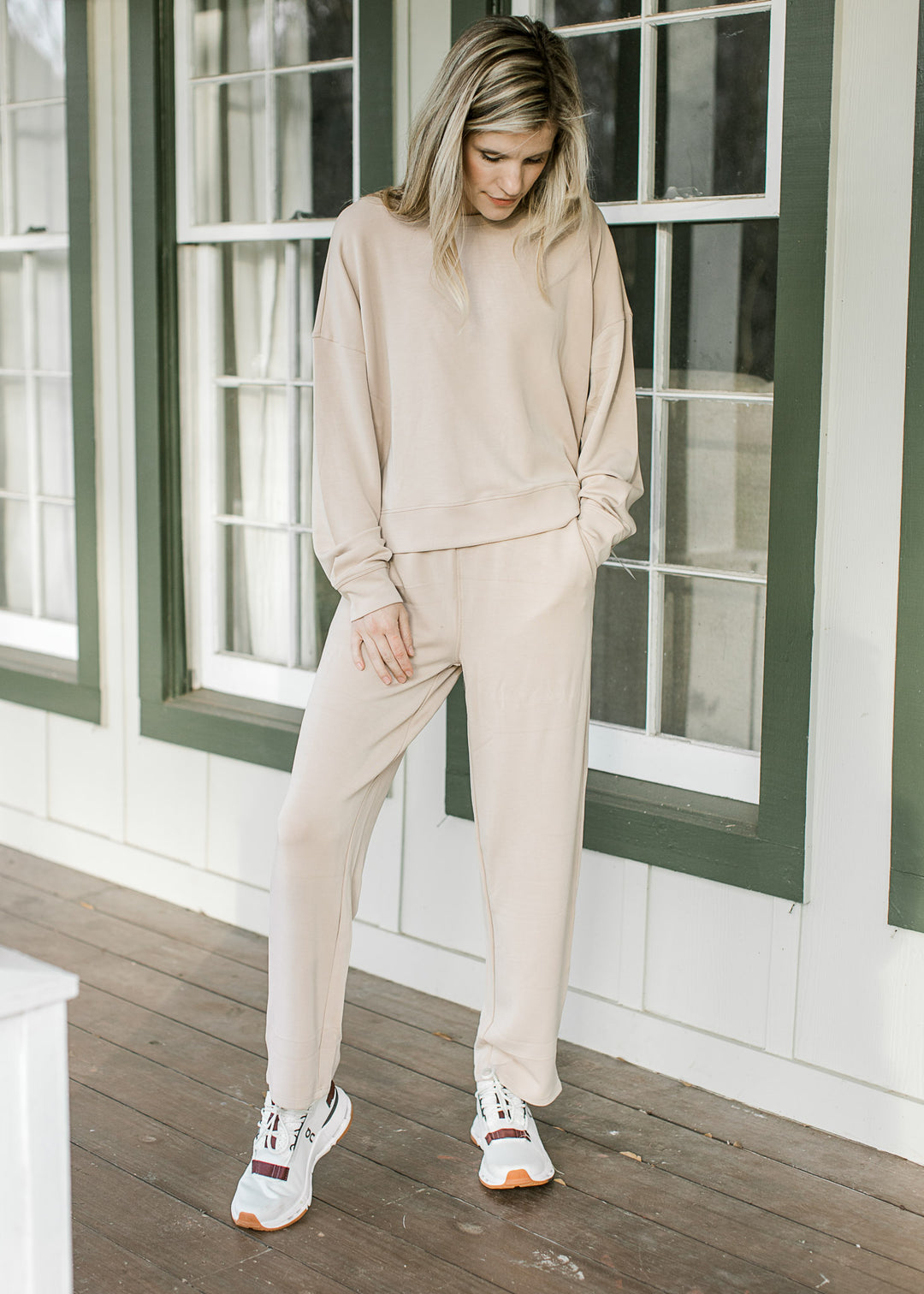 Model wearing sneakers and a cream set with a long sleeve top and straight leg pants. 