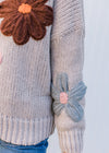 Detail view of yarn flowers on a taupe long sleeves sweater with ribbed neck, cuff and hem. 