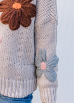 Detail view of yarn flowers on a taupe long sleeves sweater with ribbed neck, cuff and hem. 