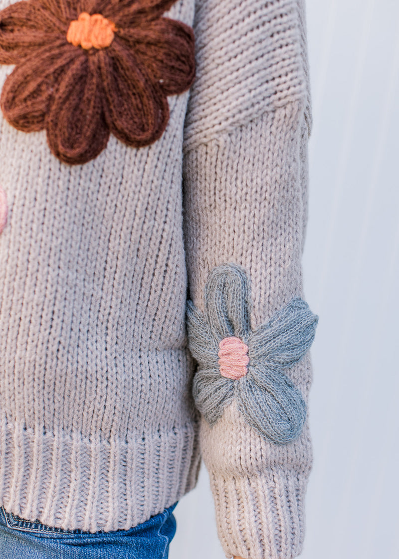 Detail view of yarn flowers on a taupe long sleeves sweater with ribbed neck, cuff and hem. 