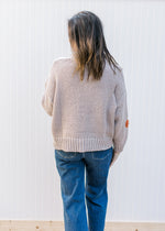 Back view of Model wearing a taupe sweater with multicolored yarn flowers and long sleeves.