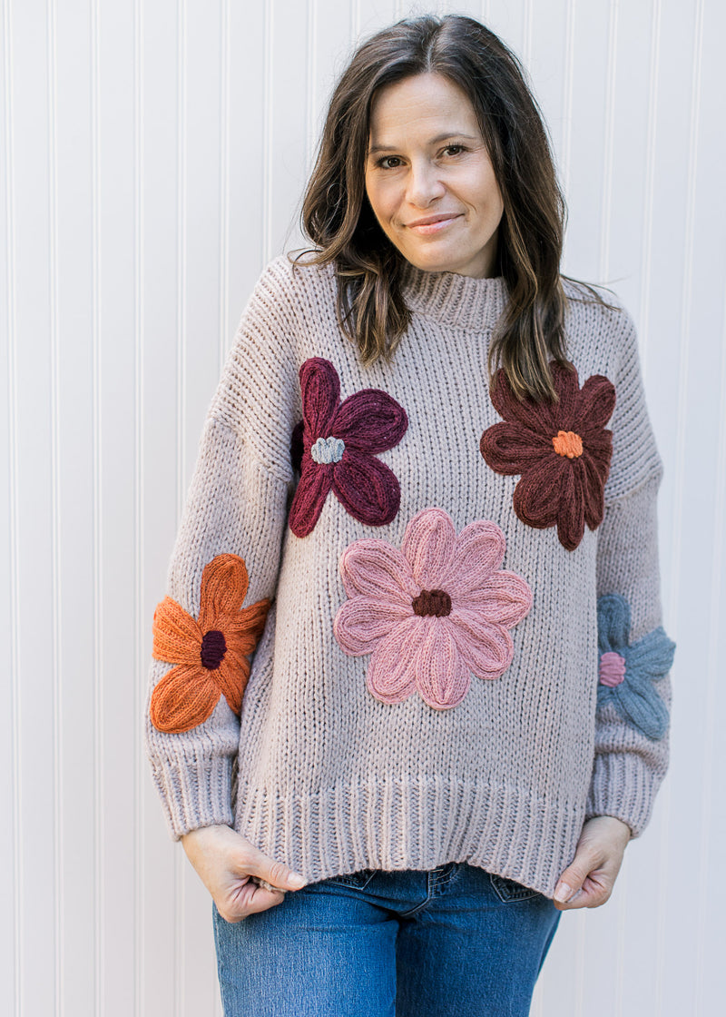 Model wearing a taupe sweater with yarn flowers, long sleeves and round neck.