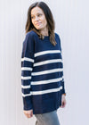 Model wearing a navy sweater with cream stripes, long sleeves and a crew neck. 