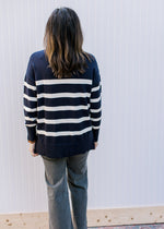 Back view of Model wearing a navy sweater with cream stripes and long sleeves.