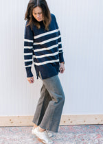 Model wearing jeans and a navy sweater with cream stripes and long sleeves.