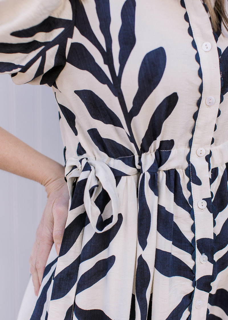 Close up of side tie closure, button front and scalloped detail on a white maxi with navy floral.