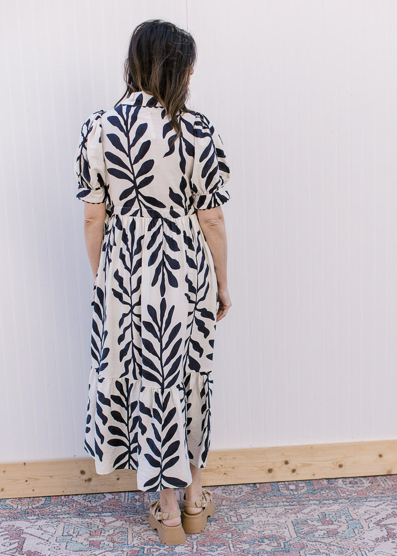 Back view of Model wearing a white dress with navy floral, short sleeves and a scalloped detail.