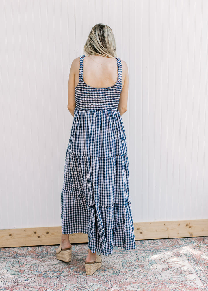 Back view of Model wearing a navy and white gingham maxi with a smocked bodice and straps.
