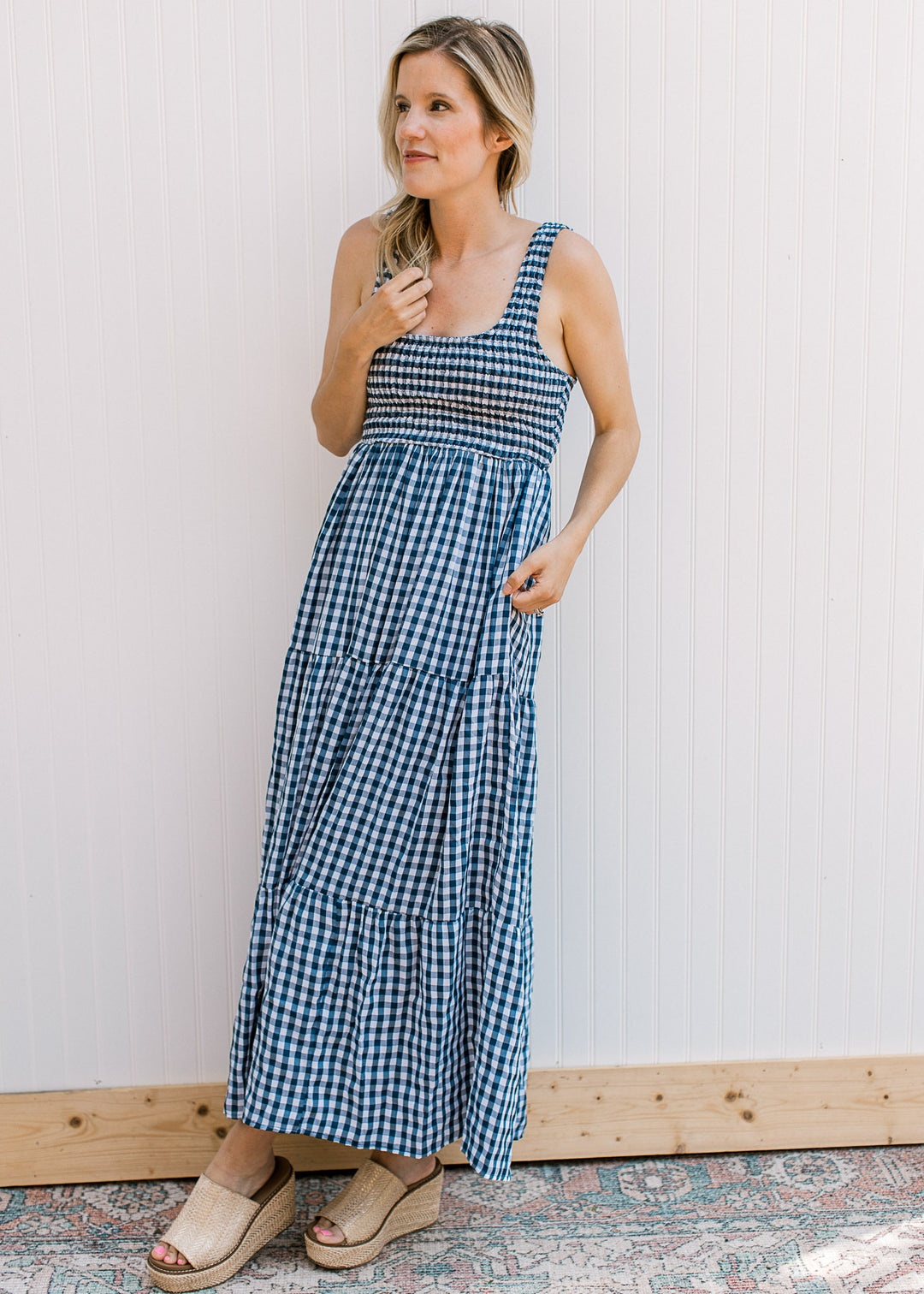 Model wearing a sleeveless navy and white gingham maxi with a smocked bodice and straps.