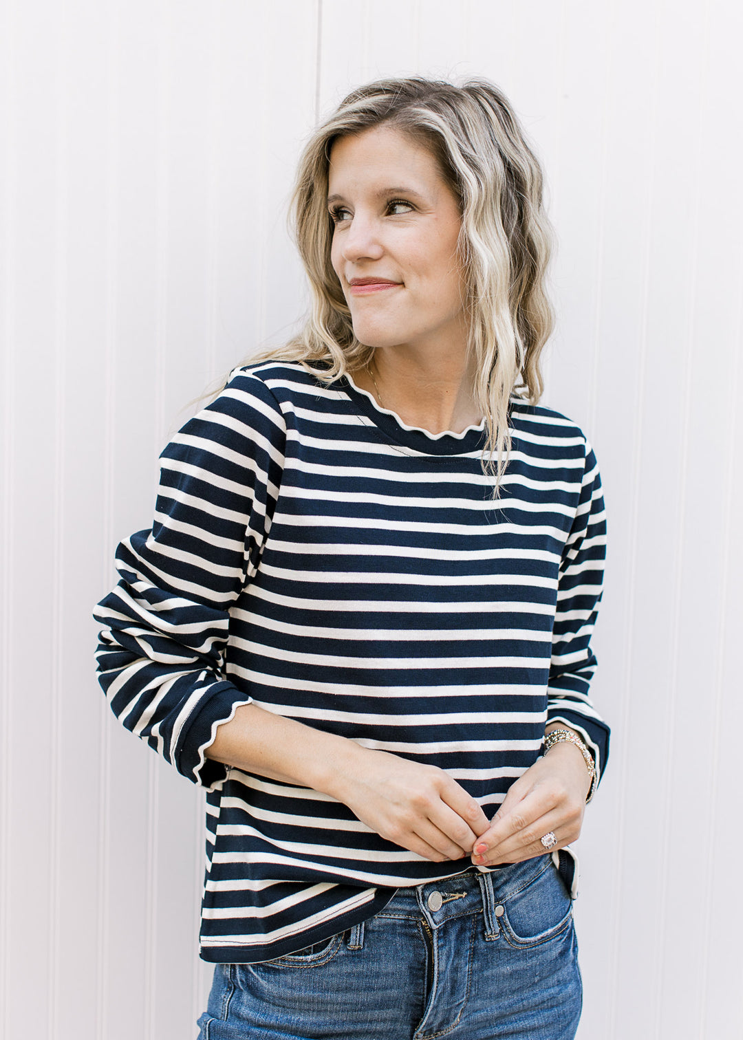 Model wearing a navy and white long sleeve stripped top with scalloping at round neck and cuff. 