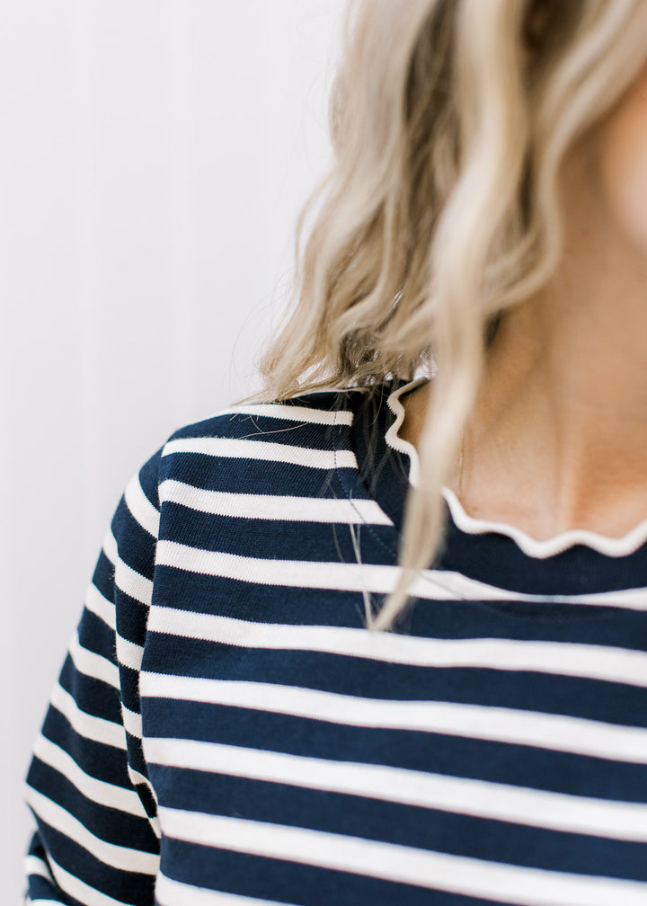 Close up of scalloped detail along the round neck of a navy and white striped long sleeve top.