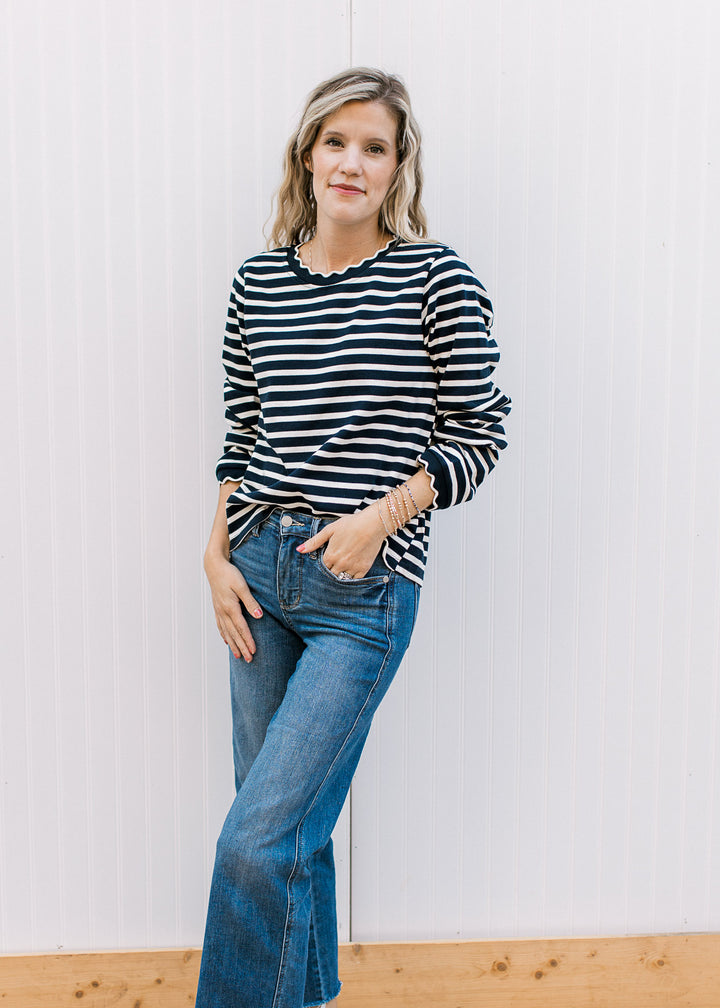 Model wearing jeans and a navy and white long sleeve stripped top with scalloping at neck and cuff. 
