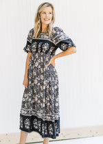 Model wearing a navy border print, midi dress with a floral pattern with short puff sleeves. 