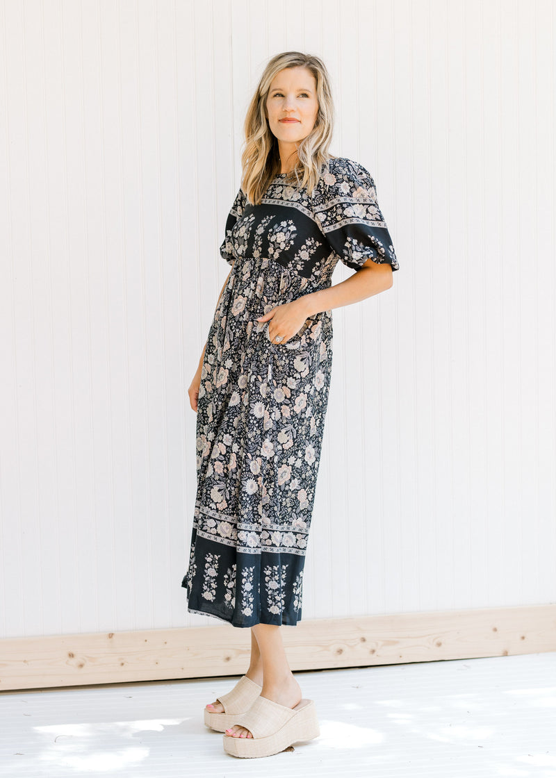 Model wearing heels and a navy midi dress with a floral pattern, square neckline and short sleeves. 
