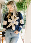 Model wearing a navy sweater with a cream daisy and cream stripes on long sleeves. 