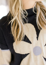 Close up of cream daisy with light blue center on a navy sweater with ribbed round neck.