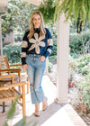 Model wearing jeans with a navy sweater with a cream daisy and cream stripes on long sleeves. 