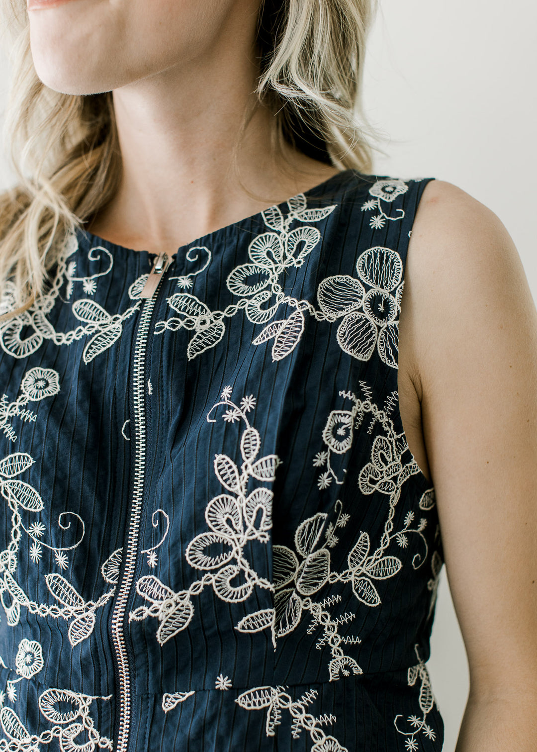 Close up of pleating at bust and front zipper on a navy sleeveless top with cream embroidery.
