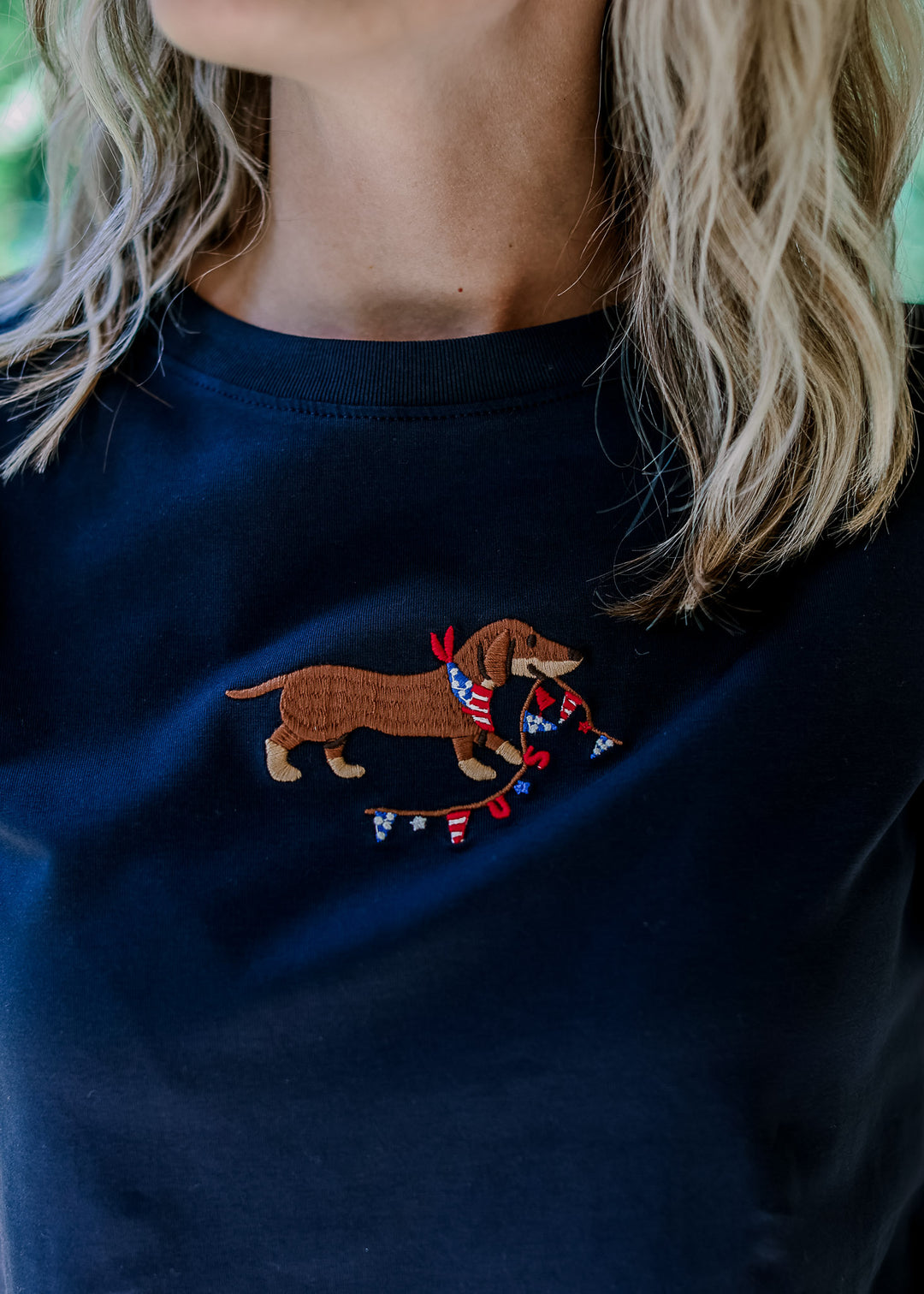 Close up of embroidered Dachshund with USA banner on a navy short sleeve top with short sleeves.