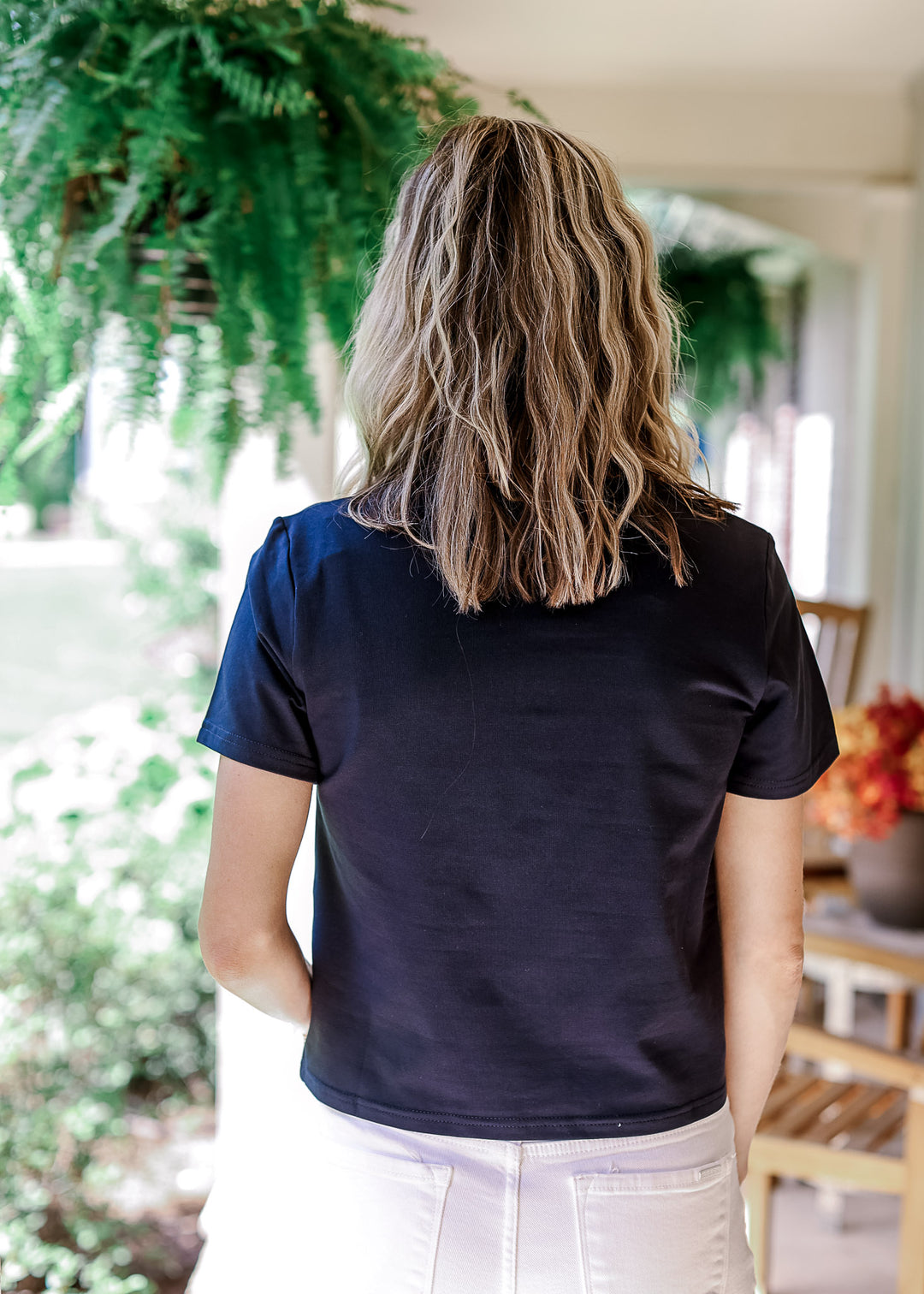Back view of Model wearing a navy top with slightly cropped fit, round neck and short sleeves.