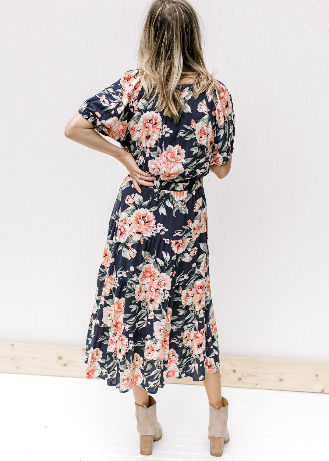 Back view of Model wearing a navy dress with rose colored floral, v-neck and short puff sleeves. 