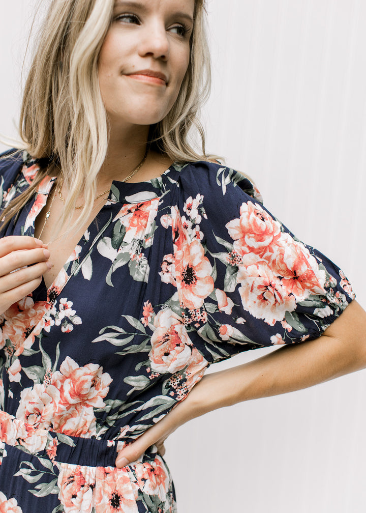 Close up of short puff sleeves and v-neck on a navy dress with a rose colored floral pattern. 