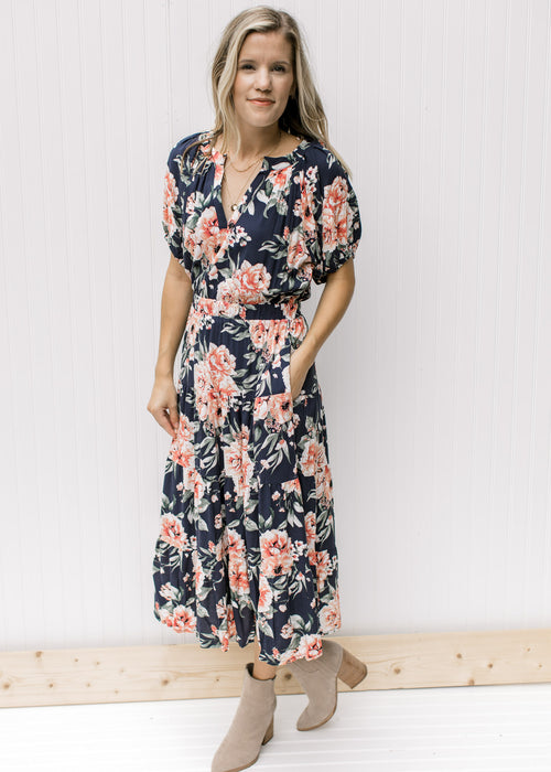 Model wearing a navy dress with rose colored floral, v-neck and short puff sleeves. 