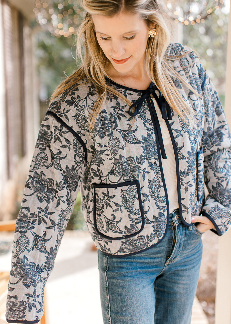 Model wearing a gray jacket with navy floral, tie closure, patch pockets and long sleeves. 