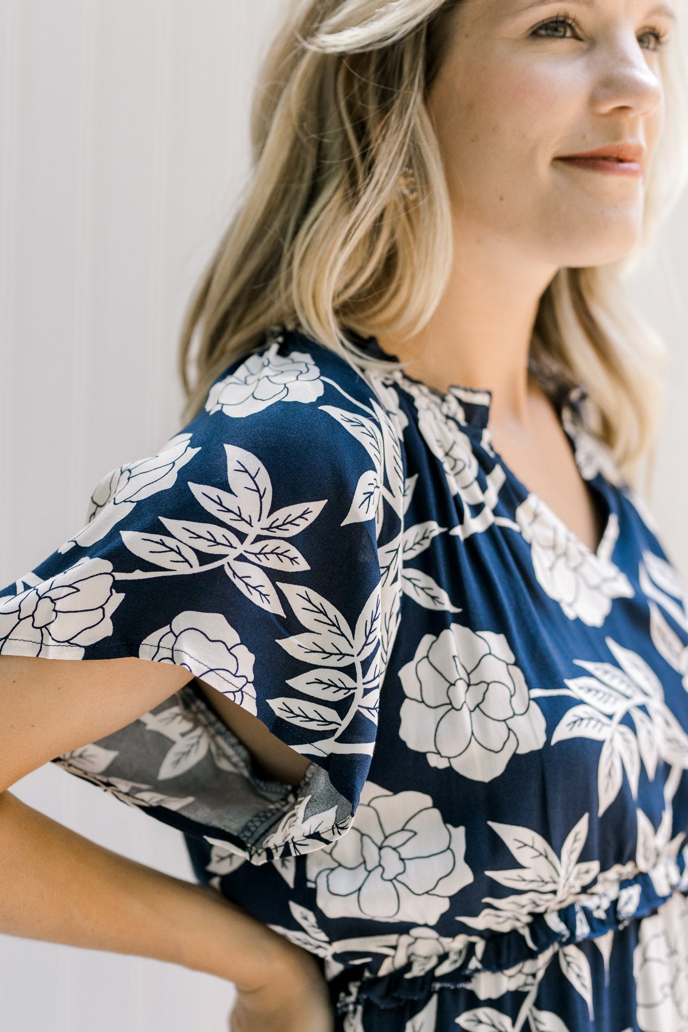 Close up view of model waring a navy dress with a white floral pattern and ruffles along the tiers. 